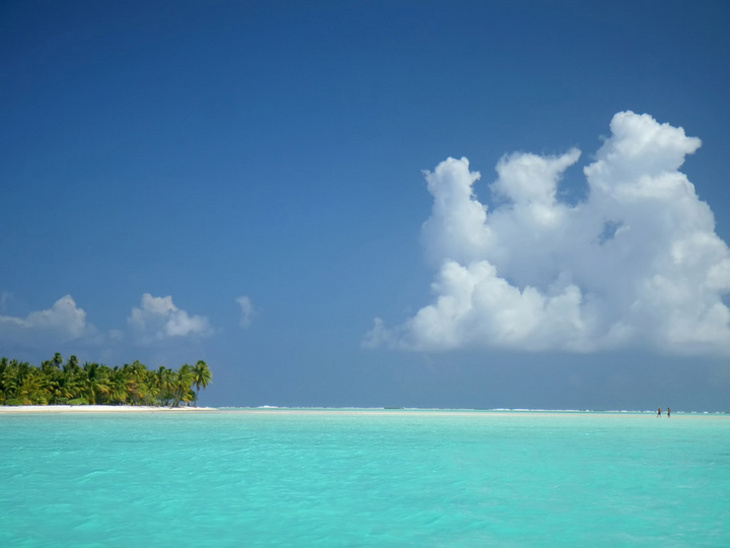 Türkises Meer mit Strand und Bäumen und ein paar Wolken am blauen Himmel