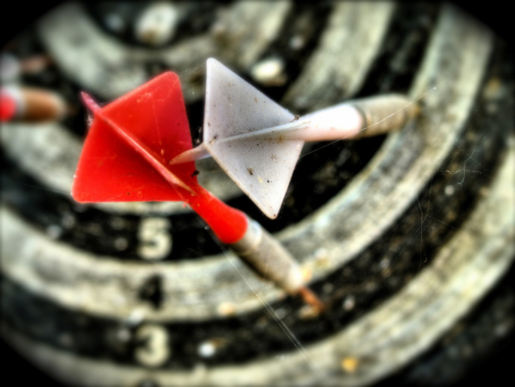 Dartscheibe, in der ein roter und ein weißer Pfeil stecken